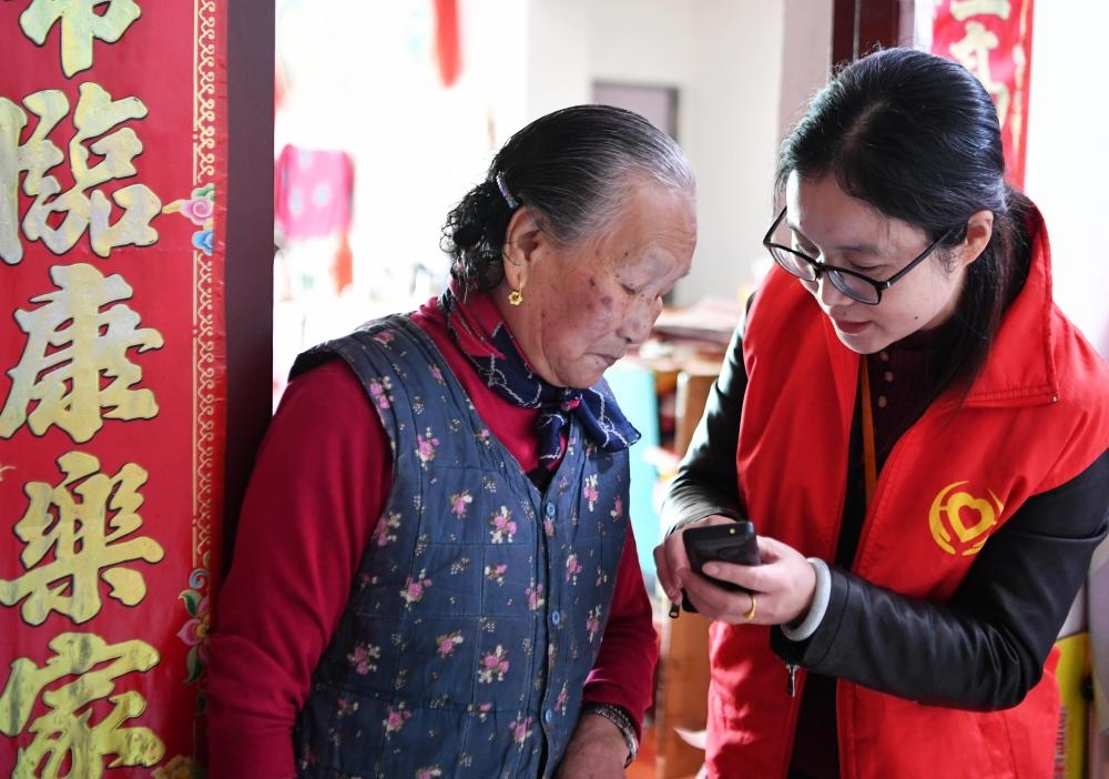 在福州市長樂區(qū)航城街道籌岐村，智慧養(yǎng)老平臺派駐社區(qū)的助老員（右）在為老人陳鳳英（左）講解養(yǎng)老定制手機的用法（2021年11月26日攝）。新華社記者 魏培全 攝
