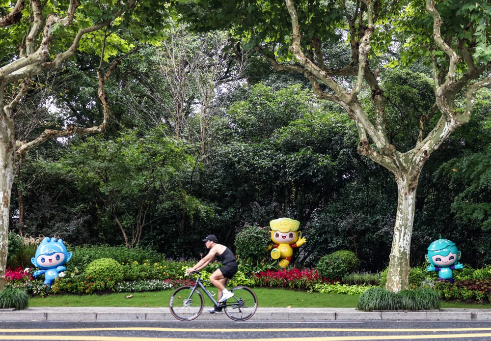 市民在杭州市南山路上一處亞運會主題吉祥物雕塑前騎自行車。