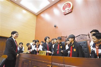 圖③：同學(xué)們穿法袍、敲法槌，爭(zhēng)做“小法官”。