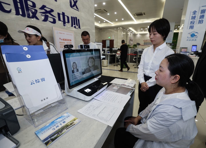 在浙江省嘉興市秀洲區(qū)王江涇鎮(zhèn)便民服務中心的“跨域通辦·云綜窗”窗口，辦理開業(yè)登記的個體工商戶（右一）通過該系統與江蘇省蘇州市吳江區(qū)盛澤鎮(zhèn)行政審批局工作人員視頻連線，進行身份讀取及材料線上審核（2024年5月9日攝）。新華社記者 徐昱 攝
