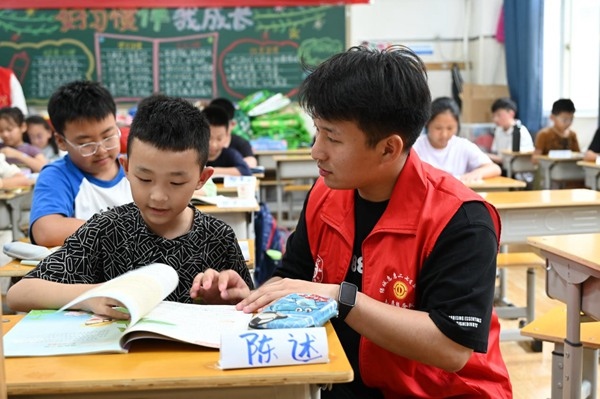 鄭州市二七區(qū)暑托班的志愿者輔導(dǎo)孩子寫作業(yè)。人民網(wǎng)記者王玉興攝