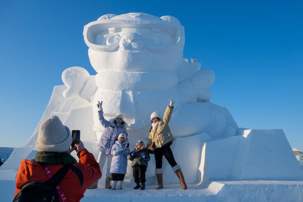 2025年1月3日，在黑龍江哈爾濱冰雪大世界園區(qū)，游客與亞冬會吉祥物雪雕“濱濱”合影